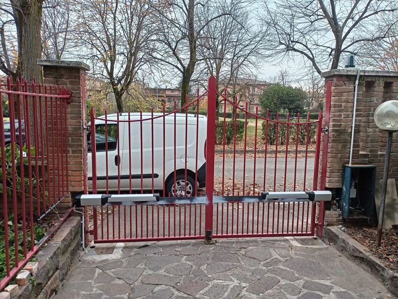 Cancello battente a due ante con un attuatore per anta, fra pilastri in mattoni, in provincia di Modena