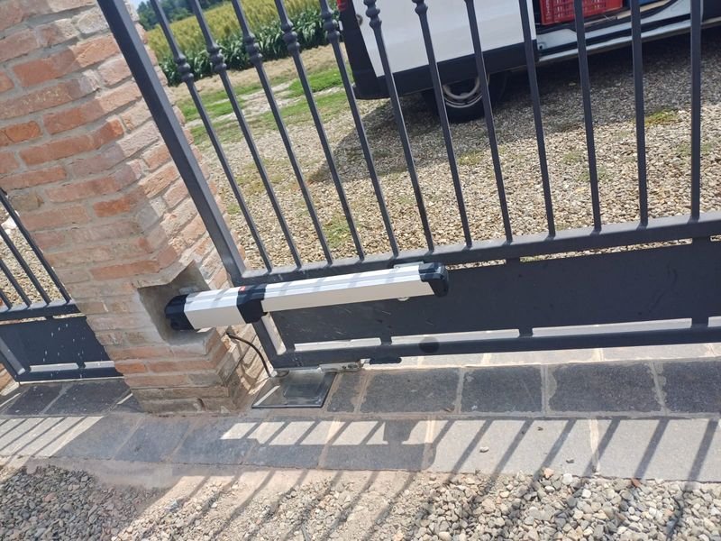 Attuatore lineare montato sull’anta di un cancello battente, fissato al pilastro in mattoni